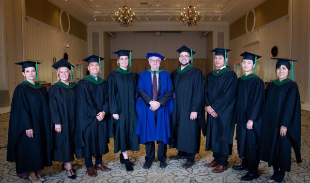 8 graduates and University president stand in a line. 
