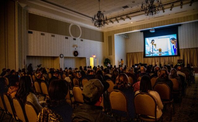 The crowd watches the slide show of the graduates' journeys at Wongu.